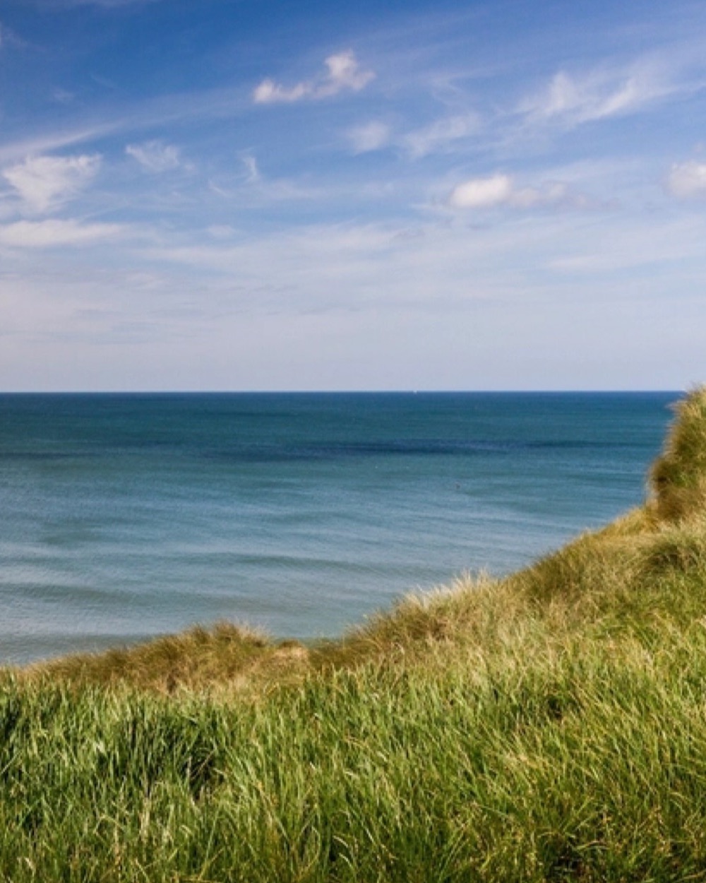 Grassy clifftop above a calm sea under a pale sky